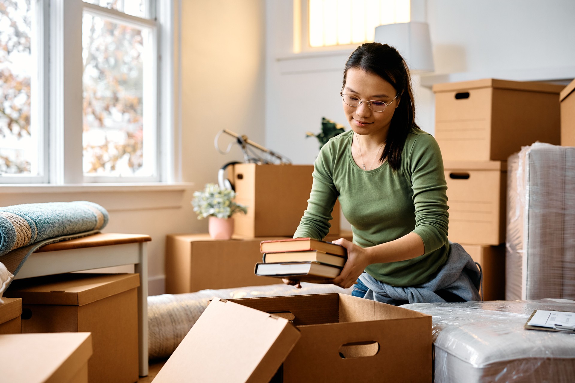 Young  Asian woman unpacking cardboard boxes while moving into a new home.